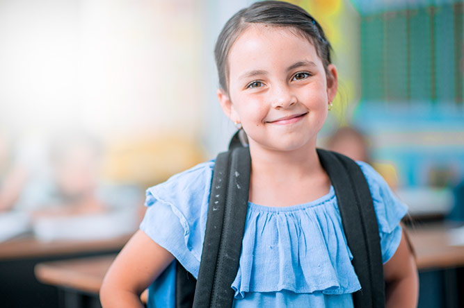 A girl smiling and carrying a bagpack