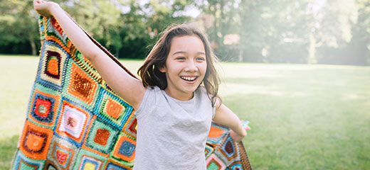 Happy little girl running with a blanket in the park